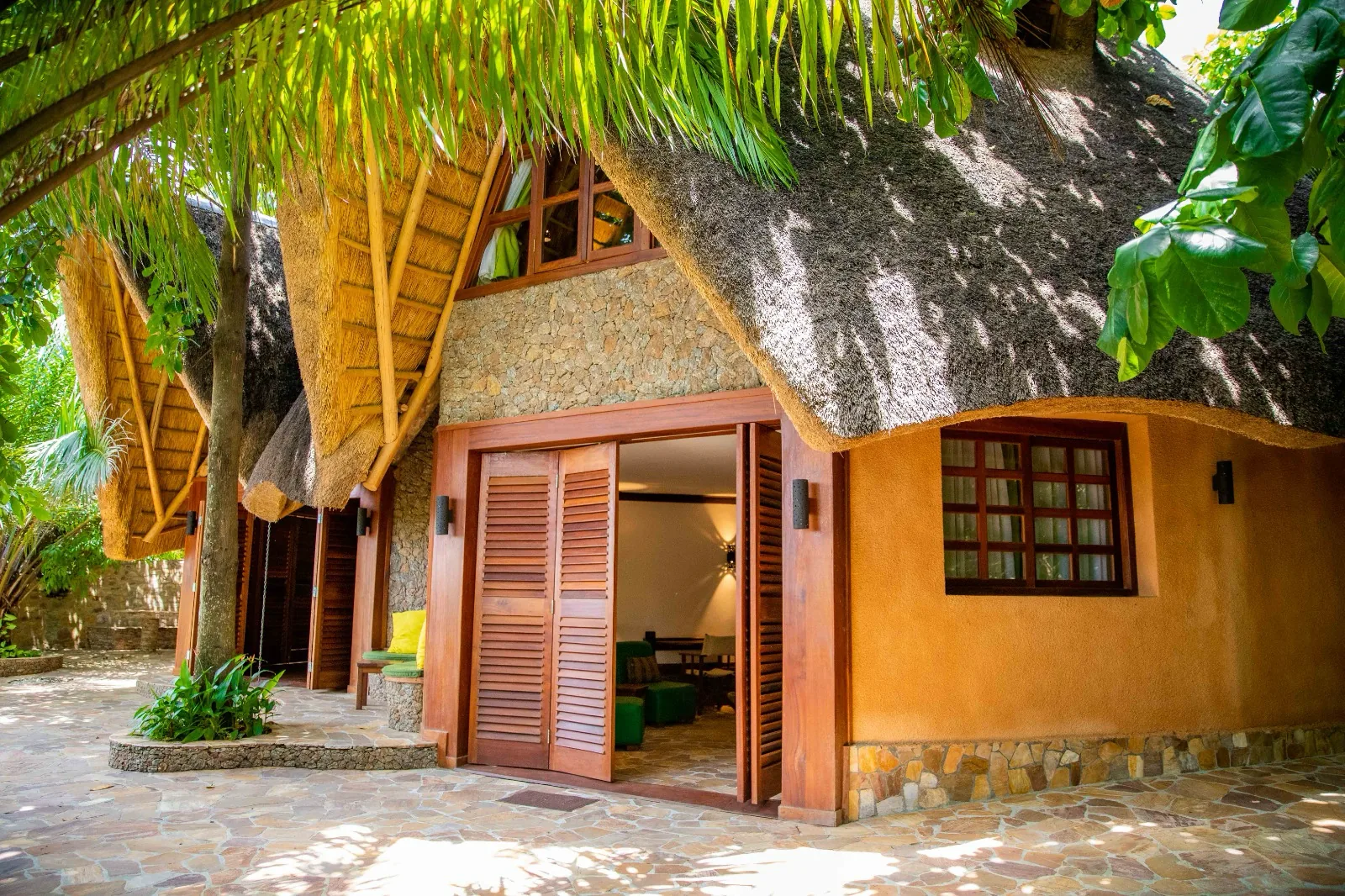 Folding wooden doors standing open on the thatched Amethyst bungalow above its sunlit flagstone terrace