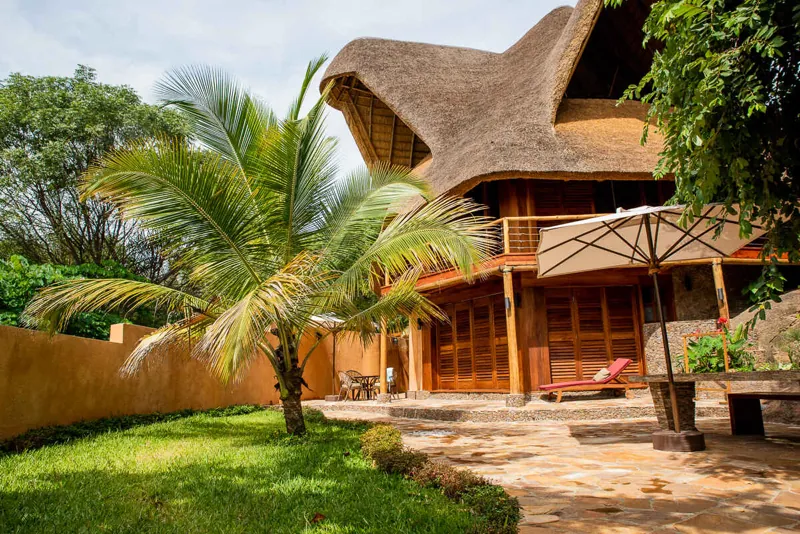 A two-storey thatched villa with a wooden balcony, sun lounger and parasol on its garden terrace