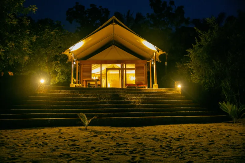 A luxury tent lit from within above the beach steps at night on Lake Tanganyika