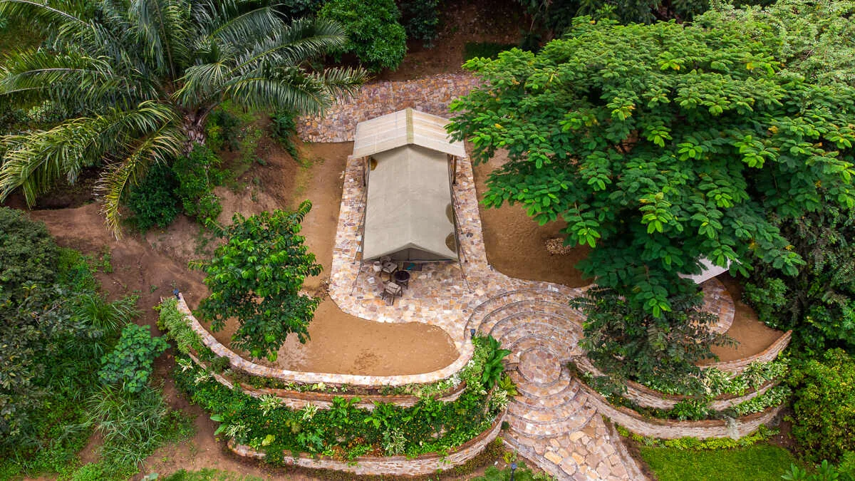 A canvas tent on curved stone terraces cut into the wooded hillside, seen from above