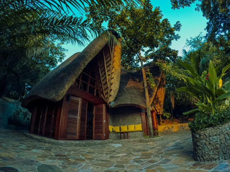 The swooping thatched roof and folding wooden louvred doors of the Malachite villa above its flagstone courtyard at dusk