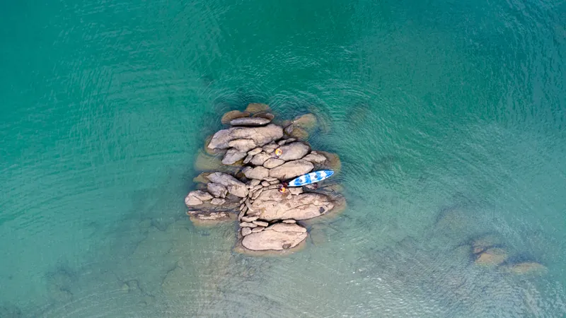 A paddleboard beside a rock outcrop in the clear turquoise water of Lake Tanganyika