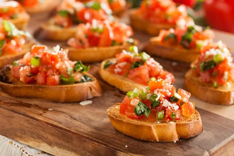 Bruschetta topped with chopped tomato and basil on a wooden board