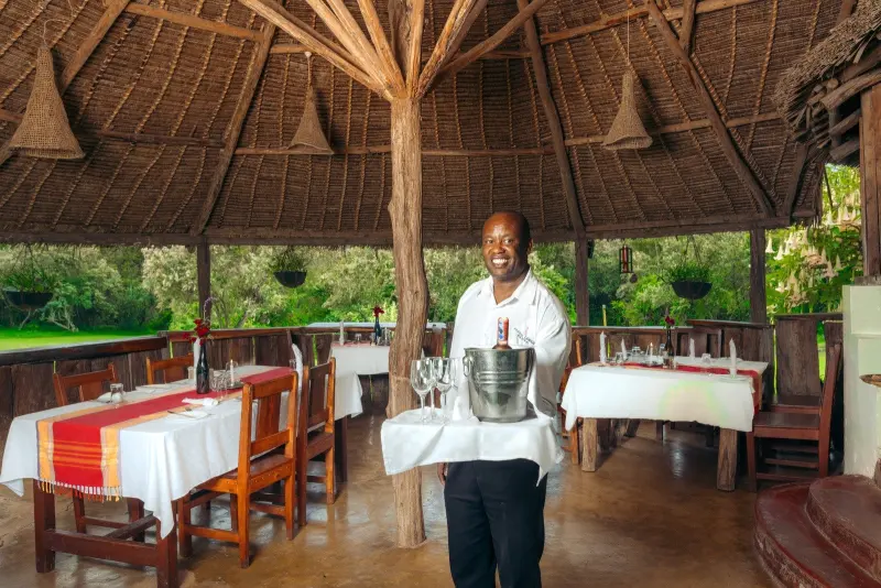 A waiter carrying a tray across the thatched restaurant, tables laid in red and white
