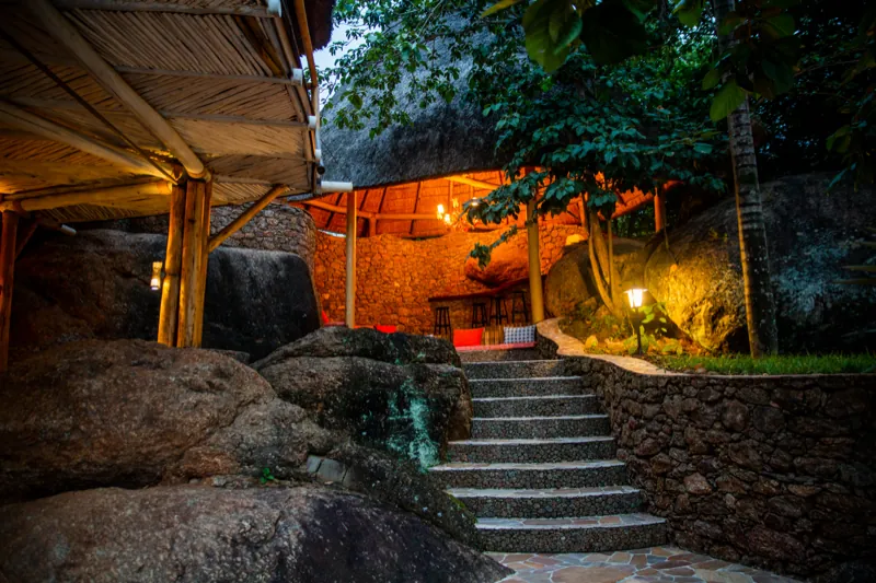 Stone steps rising to a lantern-lit bar counter set between huge granite boulders