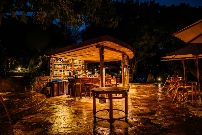 The outdoor thatched bar lit warmly at dusk, with stools, high tables and bottles lining the shelves