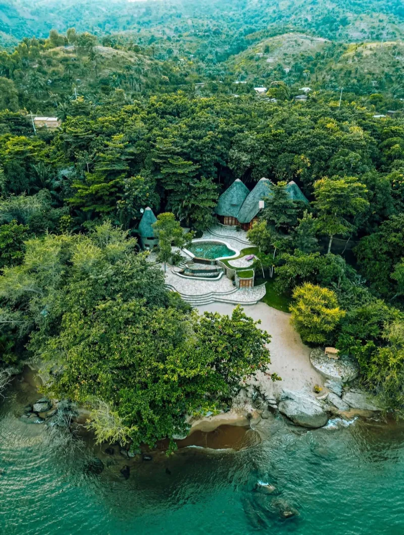 The thatched roofs of Sunstone Beach among the trees on the shore of Lake Tanganyika, seen from the air