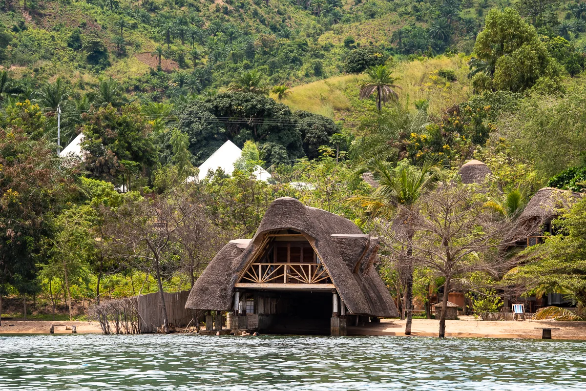The wooded shoreline of Sunstone Beach seen from the water, thatched roofs among the trees