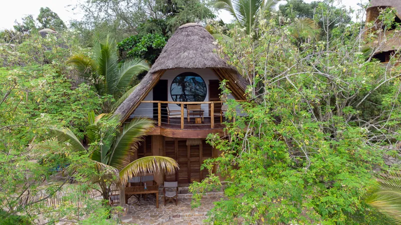 A two-storey thatched villa with a round window and a balcony above the gardens