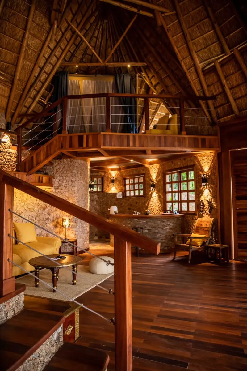 A double-height thatched living room with stone walls, timber floors and a mezzanine bedroom above